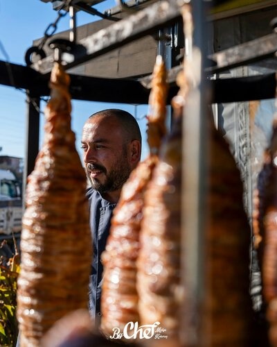 ByChef tezgâhında sıraya dizilmiş kokoreçler ve arkada Timur Evkuran
